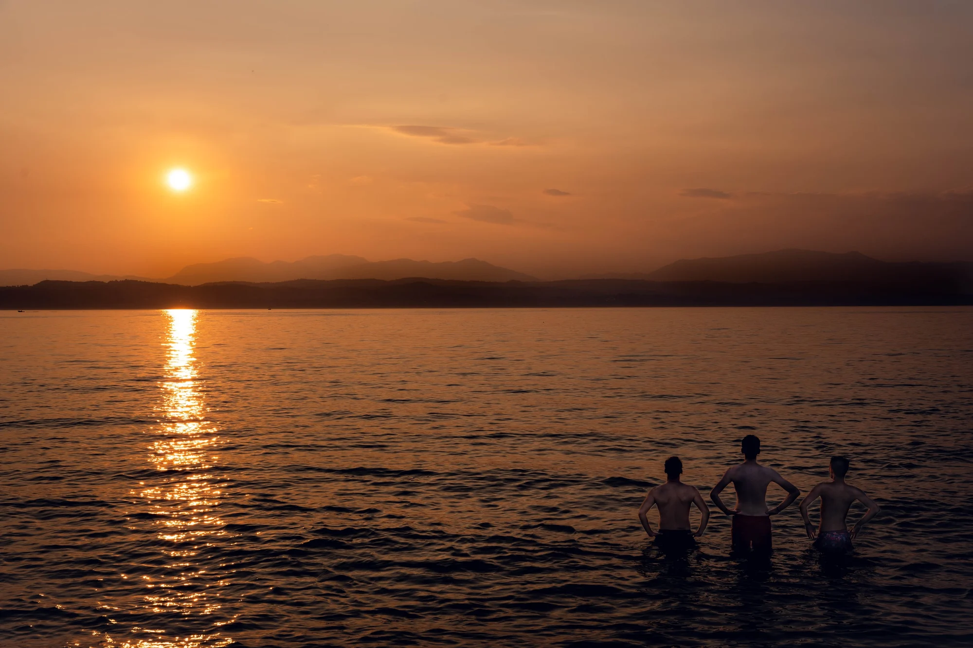 Tre ragazzi in acqua guardano il tramonto sul lago