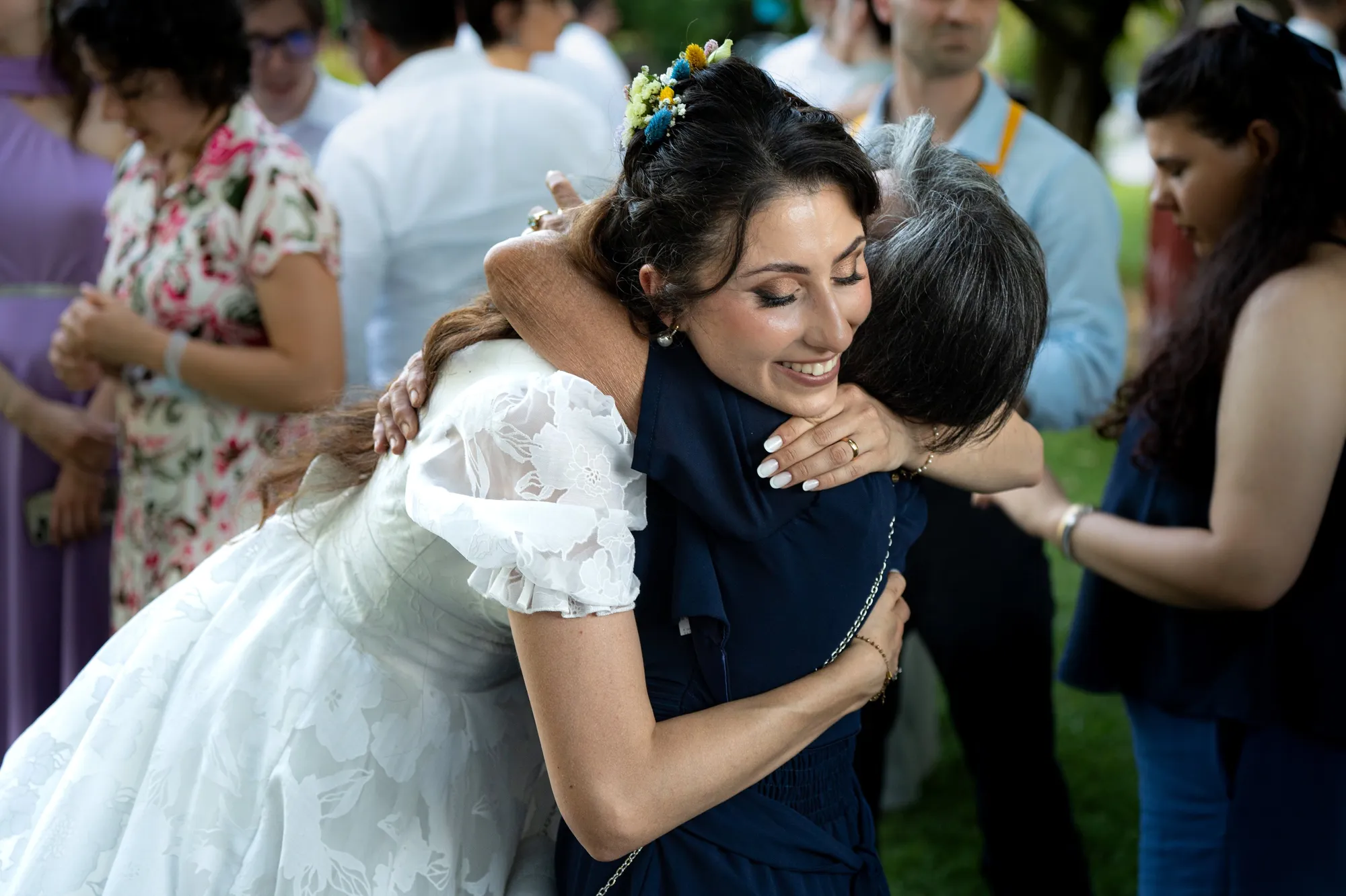 La sposa abbraccia commossa un'invitata tra la gente, sorriso e occhi lucidi