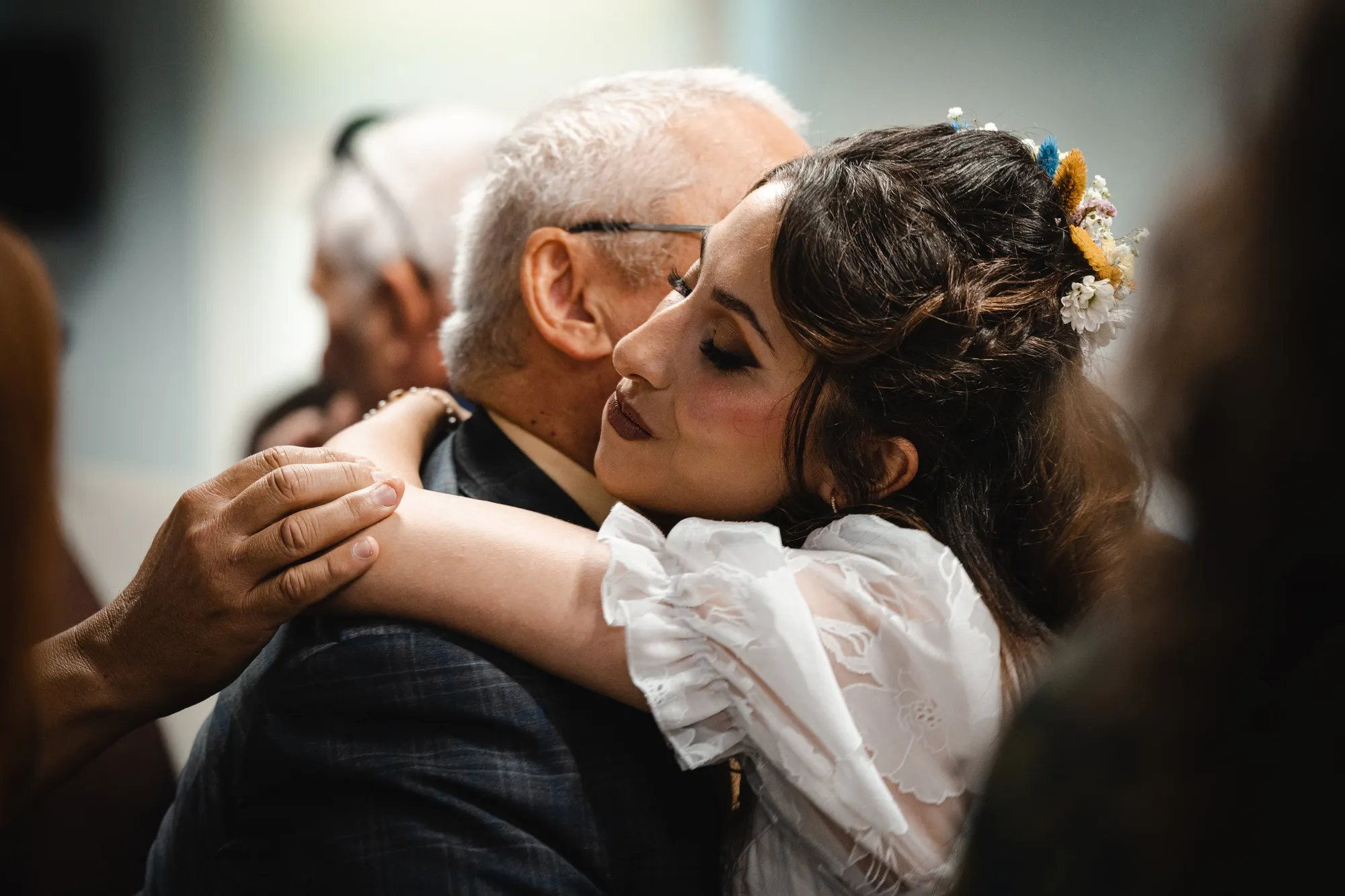 La sposa si china ad abbracciare un uomo anziano seduto tra gli invitati