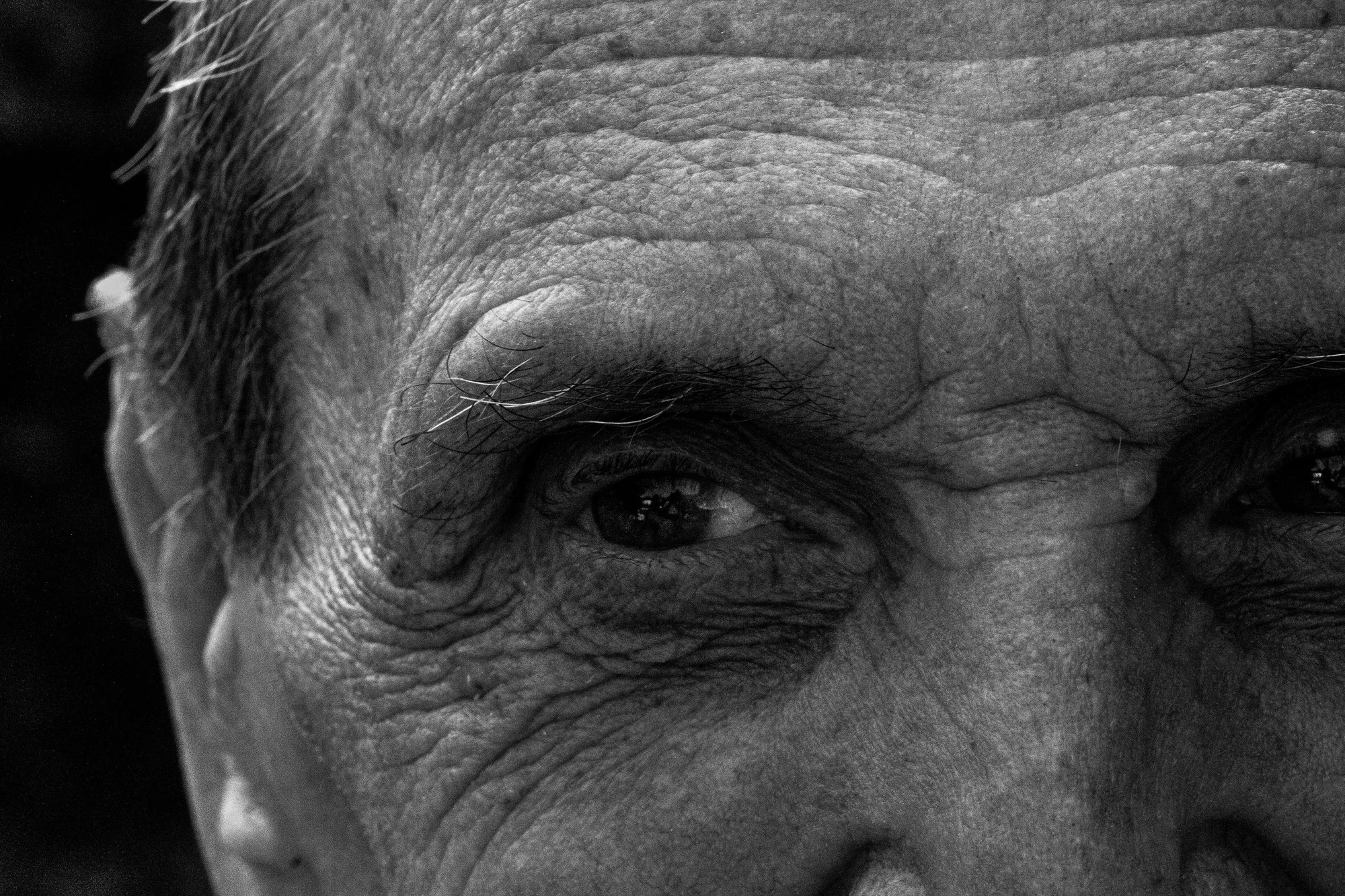 In bianco e nero, primo piano ravvicinato del volto di un uomo anziano: fronte e contorno occhi segnati da rughe profonde